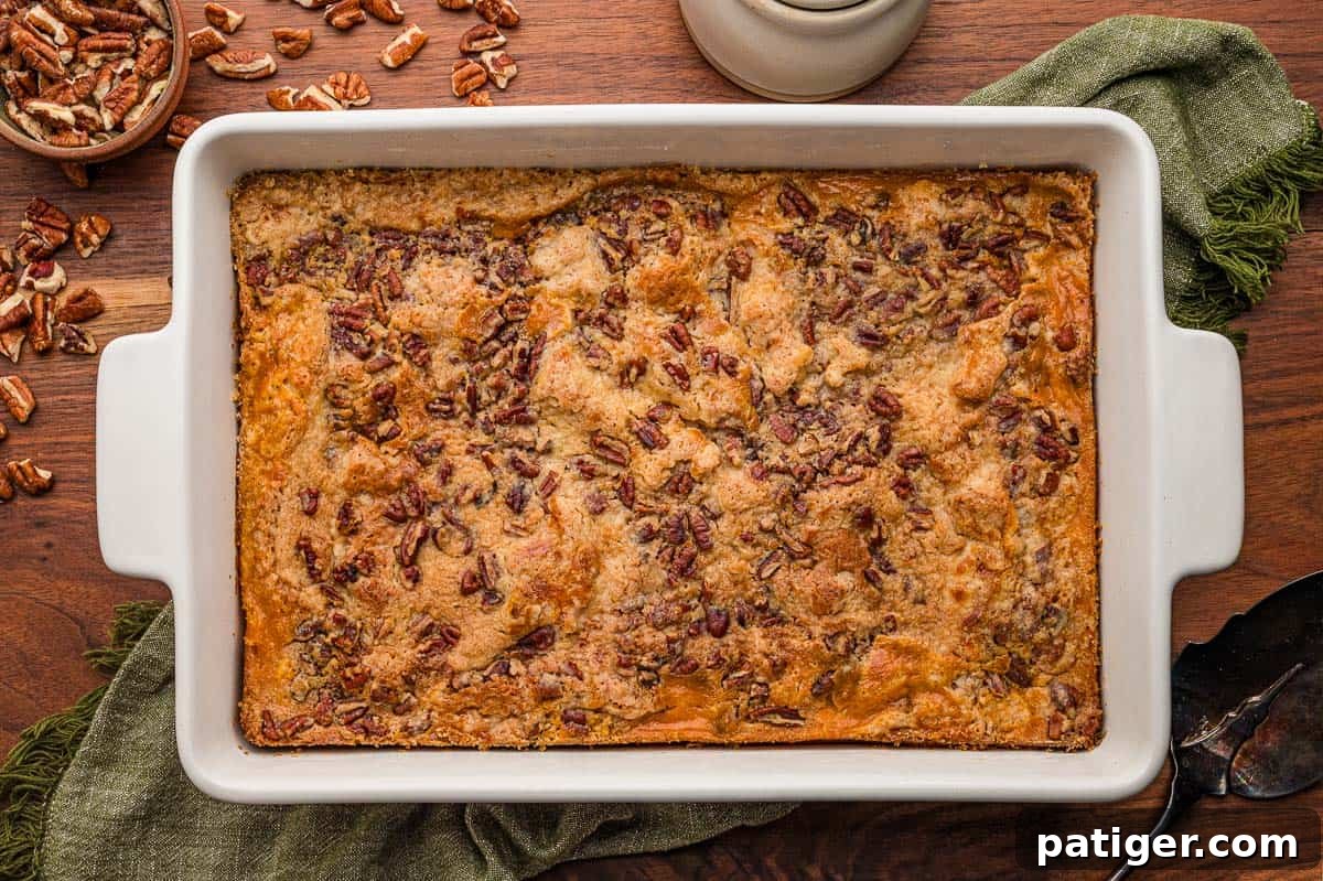 Pumpkin dump cake baked in a white 9x13 dish with a pecan topping, a green napkin and pecans alongside.