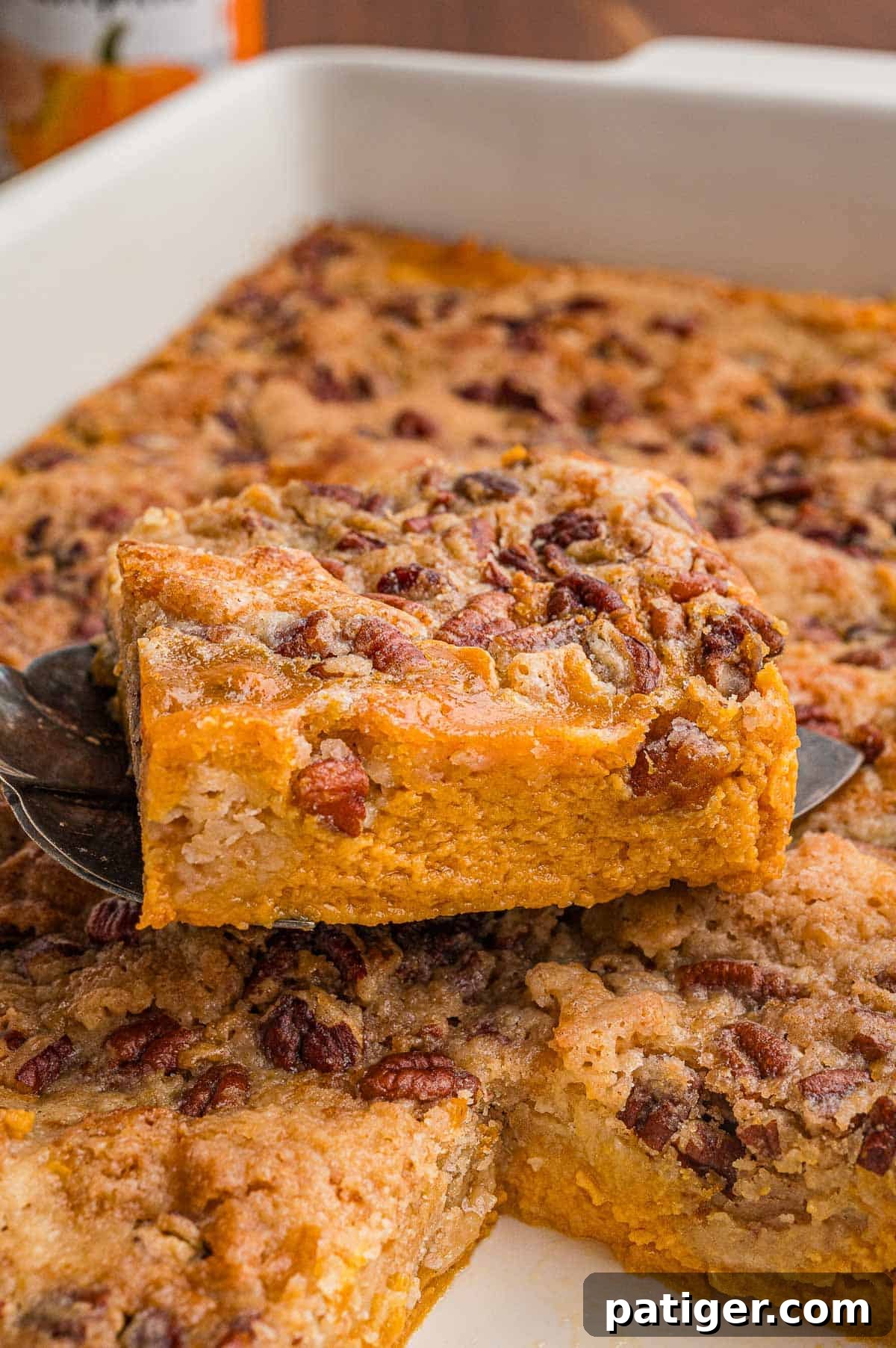 A square lifted on a serving spatula showing the orange pumpkin layer under a pecan crumb topping.