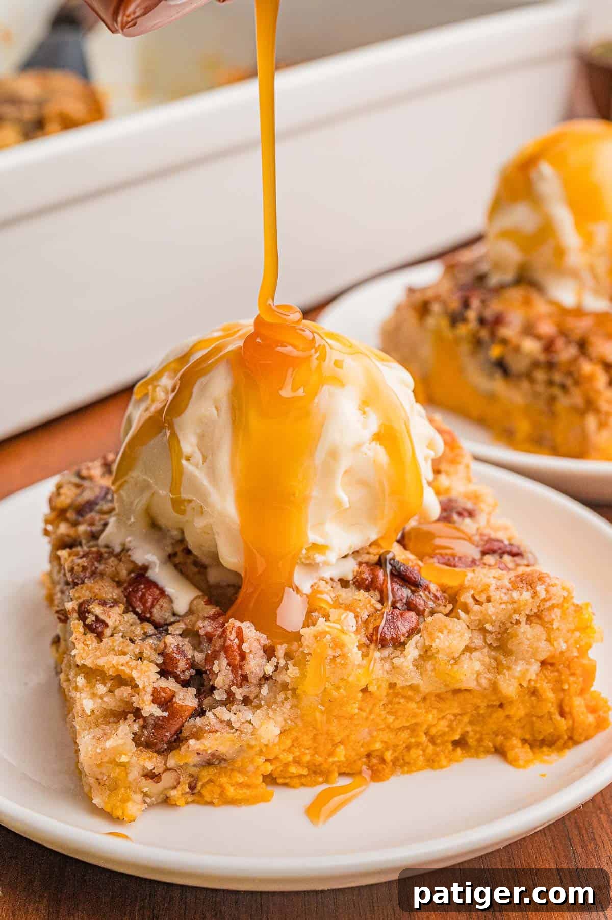 Caramel sauce being poured over a scoop of vanilla ice cream on a square of pumpkin cake.