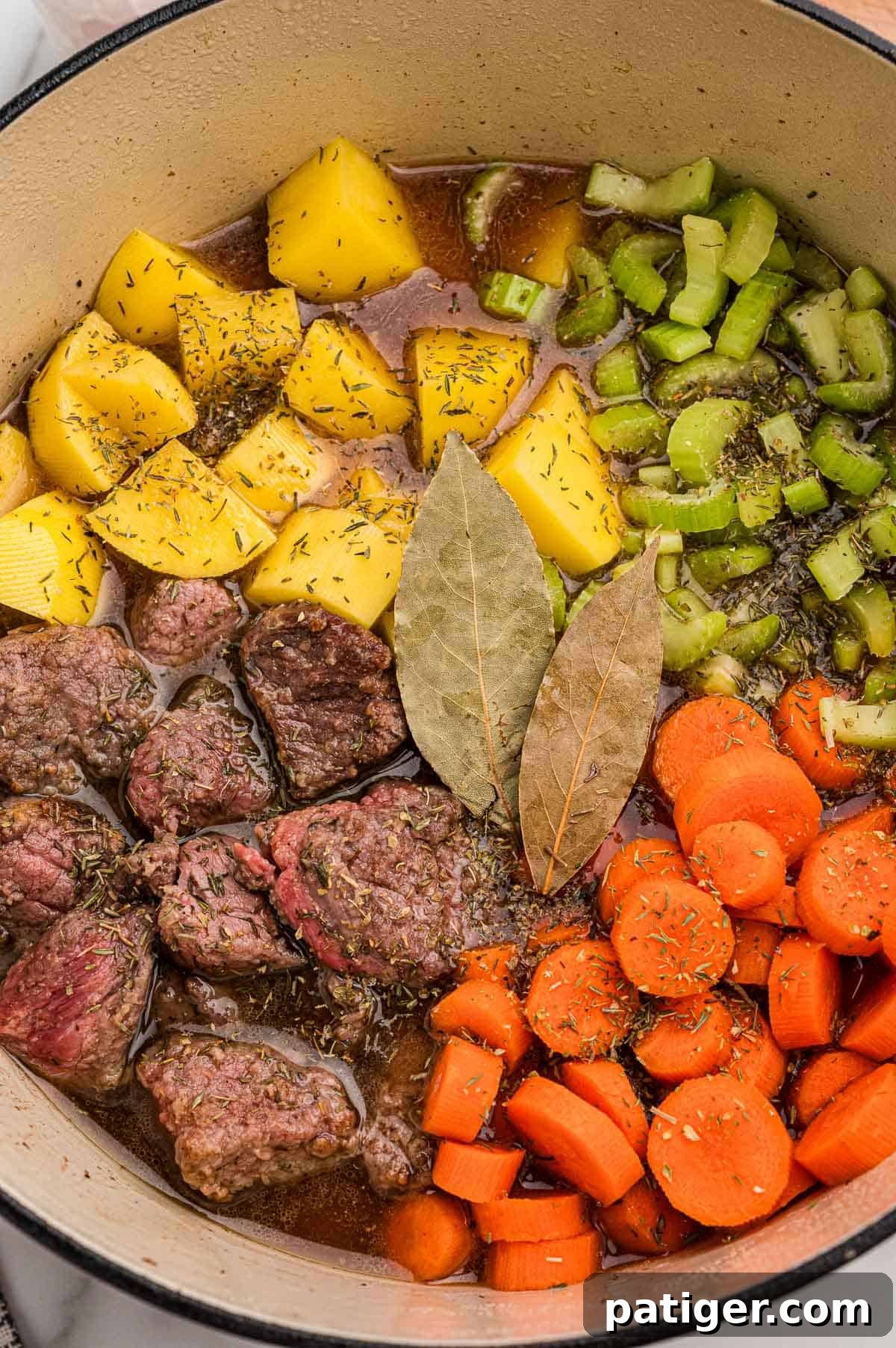Classic Hearty Beef Stew Recipe with Tender Braised Beef 5 Browned beef, potatoes, celery, carrots, and two bay leaves arranged in a Dutch oven before simmering.