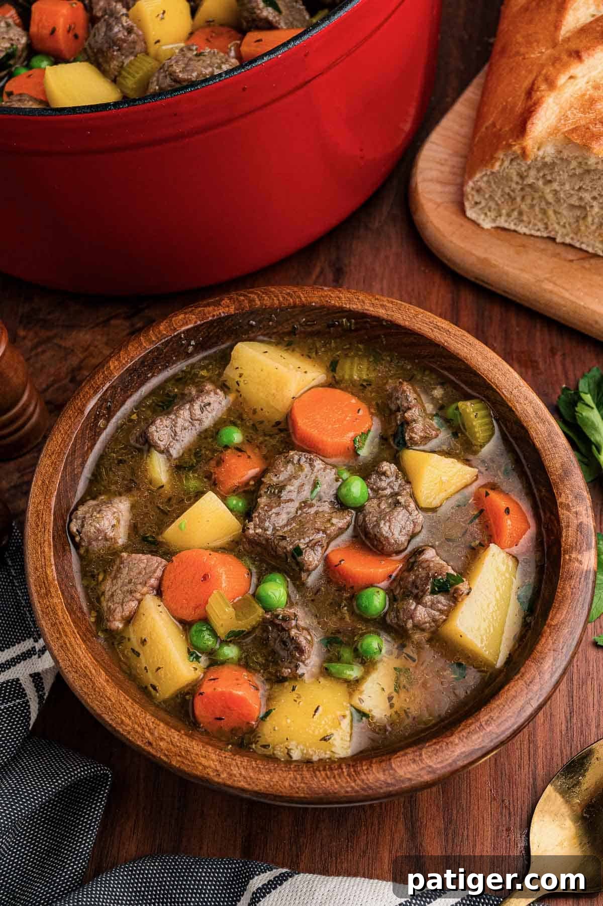 Classic Hearty Beef Stew Recipe with Tender Braised Beef 7 Beef stew served in a wooden bowl with a gold spoon, crusty bread and the pot behind it.