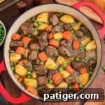 Overhead view of a red Dutch oven filled with beef, potatoes, carrots, celery, and peas.