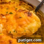Close-up of a spoonful of creamy mashed potatoes covered in browned melted cheddar and parsley.