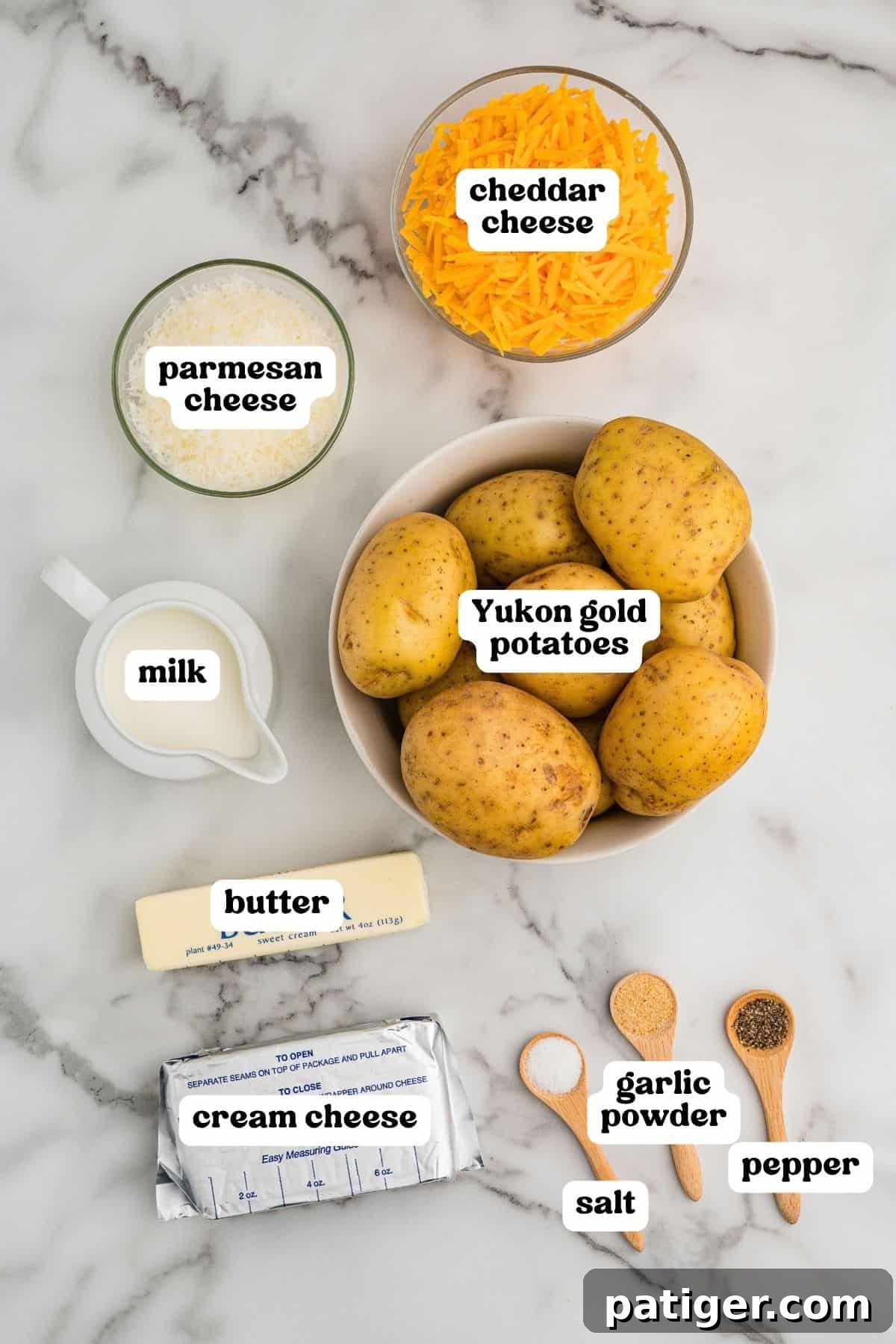 Labeled ingredients on a marble counter: Yukon Gold potatoes, shredded cheddar, Parmesan, milk, butter, cream cheese, garlic powder, salt, and pepper.