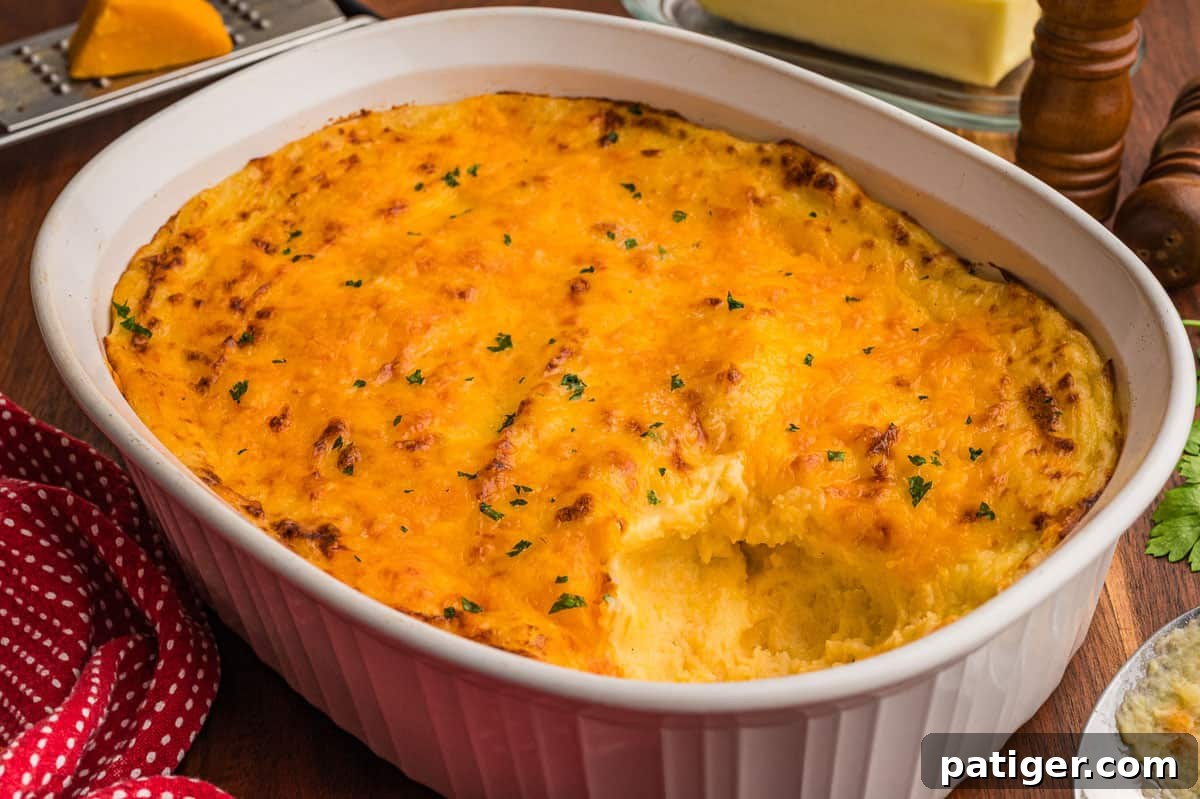 Cheesy mashed potatoes baked in a white oval casserole dish with a golden cheddar top and one scoop taken out.