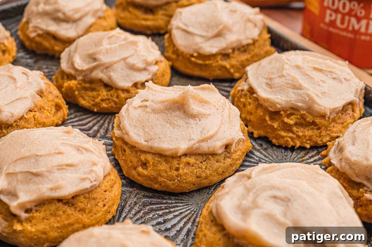Pumpkin cookies with cream cheese frosting on a patterned metal tray with a can of pumpkin behind.