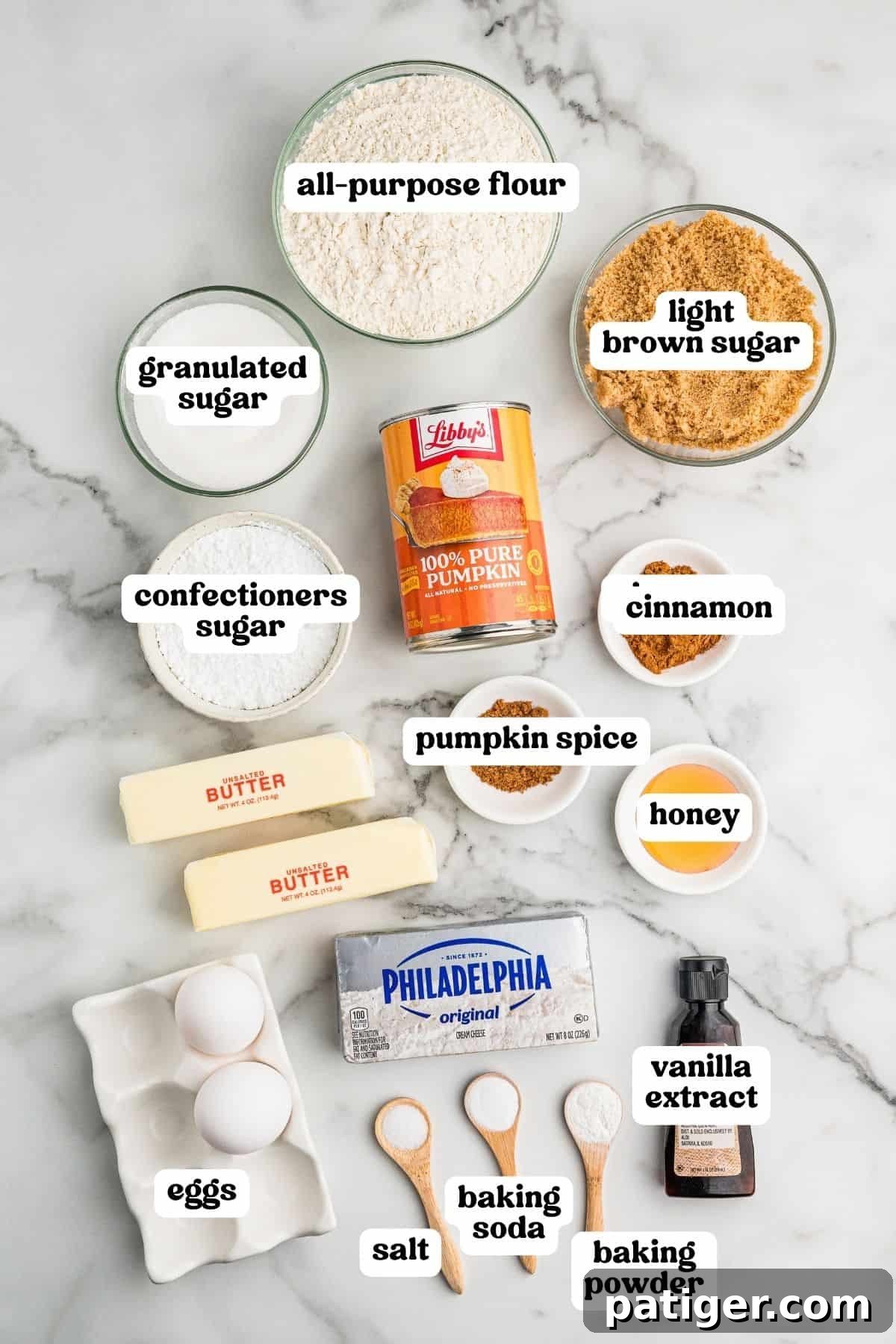 Ingredients on a marble counter: flour, sugars, pumpkin puree, spices, honey, butter, cream cheese, eggs, vanilla, salt, and leaveners.