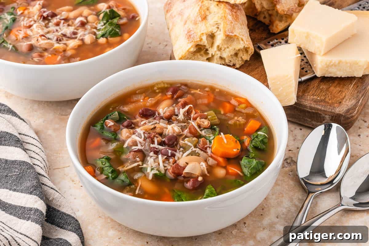 Bowl of slow cooker bean soup topped with Parmesan, with crusty bread, a block of Parmesan, and two spoons beside it.
