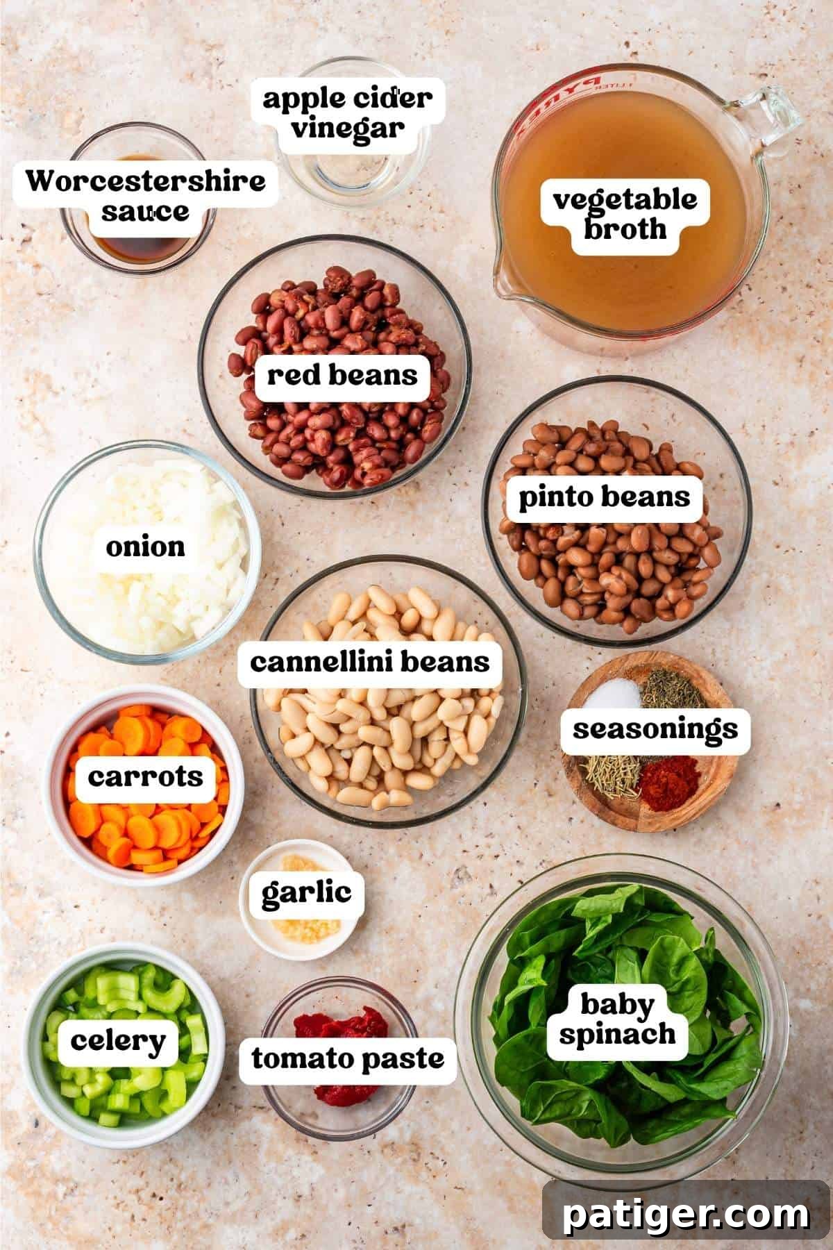Labeled ingredients in bowls: canned red, pinto, and cannellini beans, onion, carrots, celery, garlic, spinach, tomato paste, seasonings, Worcestershire sauce, apple cider vinegar, and vegetable broth.