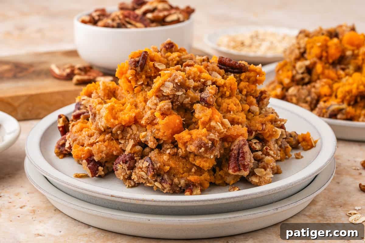 A serving of sweet potato casserole with pecan streusel on a stack of white plates.
