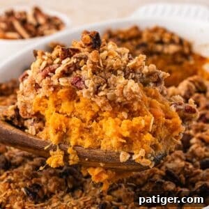 Close-up of a wooden spoon holding creamy sweet potato filling under a crumbly pecan oat topping.