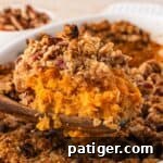 Close-up of a wooden spoon holding creamy sweet potato filling under a crumbly pecan oat topping.