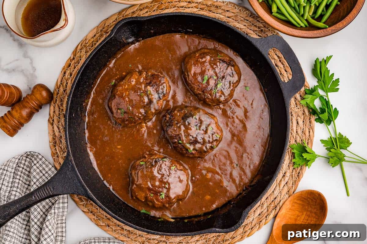 Overhead view of four patties in gravy in a cast iron skillet.