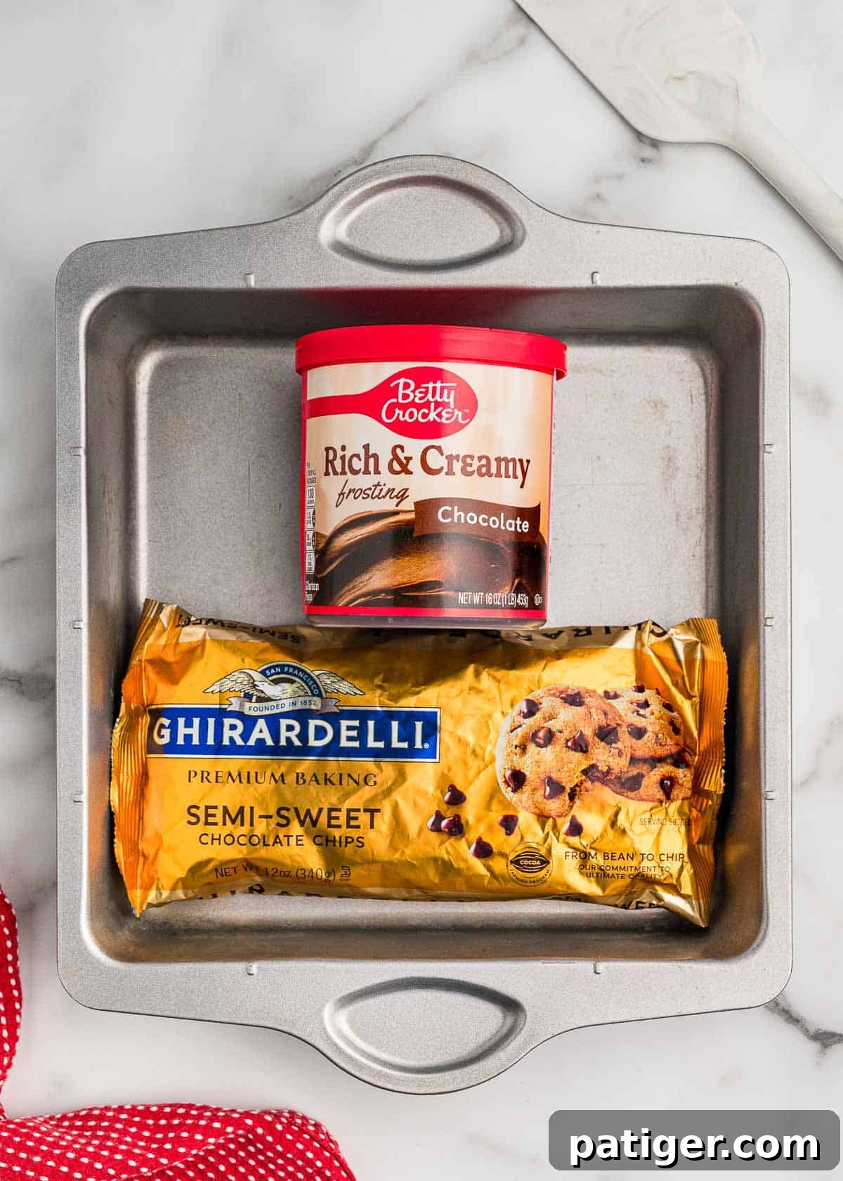 Two-Ingredient Chocolate Fudge Recipe 4 Ingredients in a square metal pan: a tub of Betty Crocker Rich & Creamy chocolate frosting and a bag of Ghirardelli semi-sweet chocolate chips.